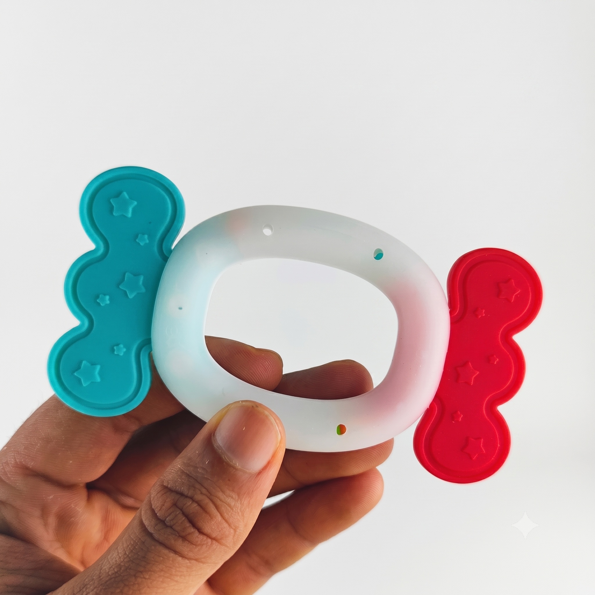 Hand holding a silicone teether with blue and red accents on a white background