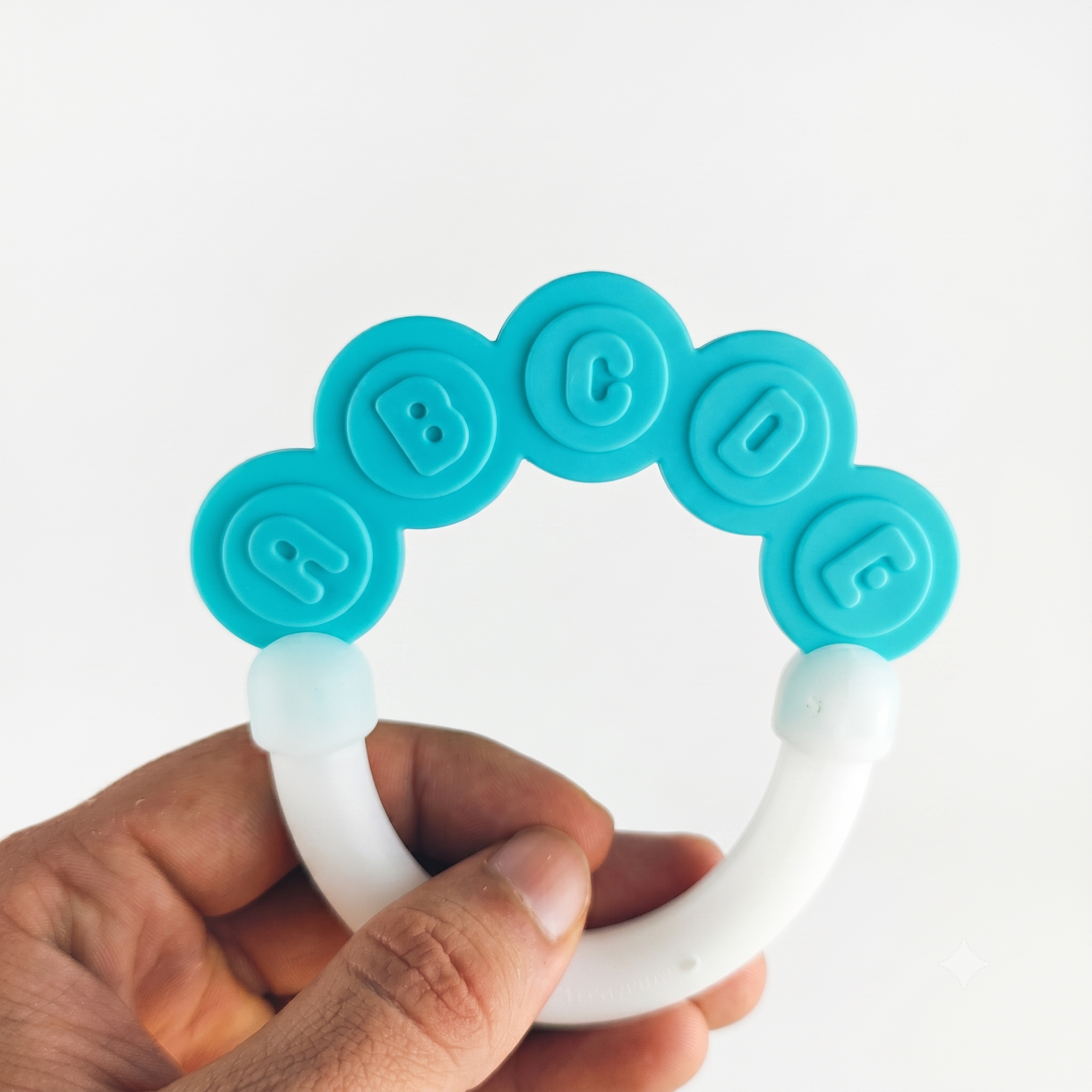 Teething ring with blue and white design held by a hand on a white background