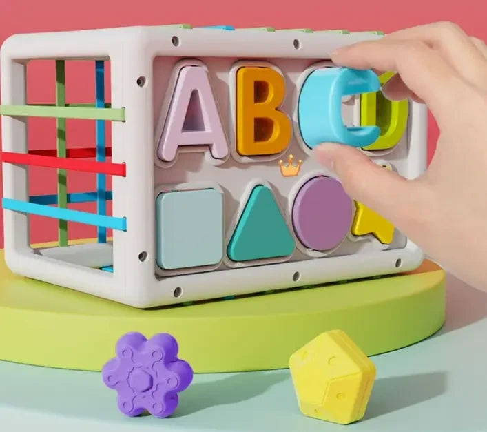 Colorful toy with letters and shapes, hand interacting with it on a pink background
