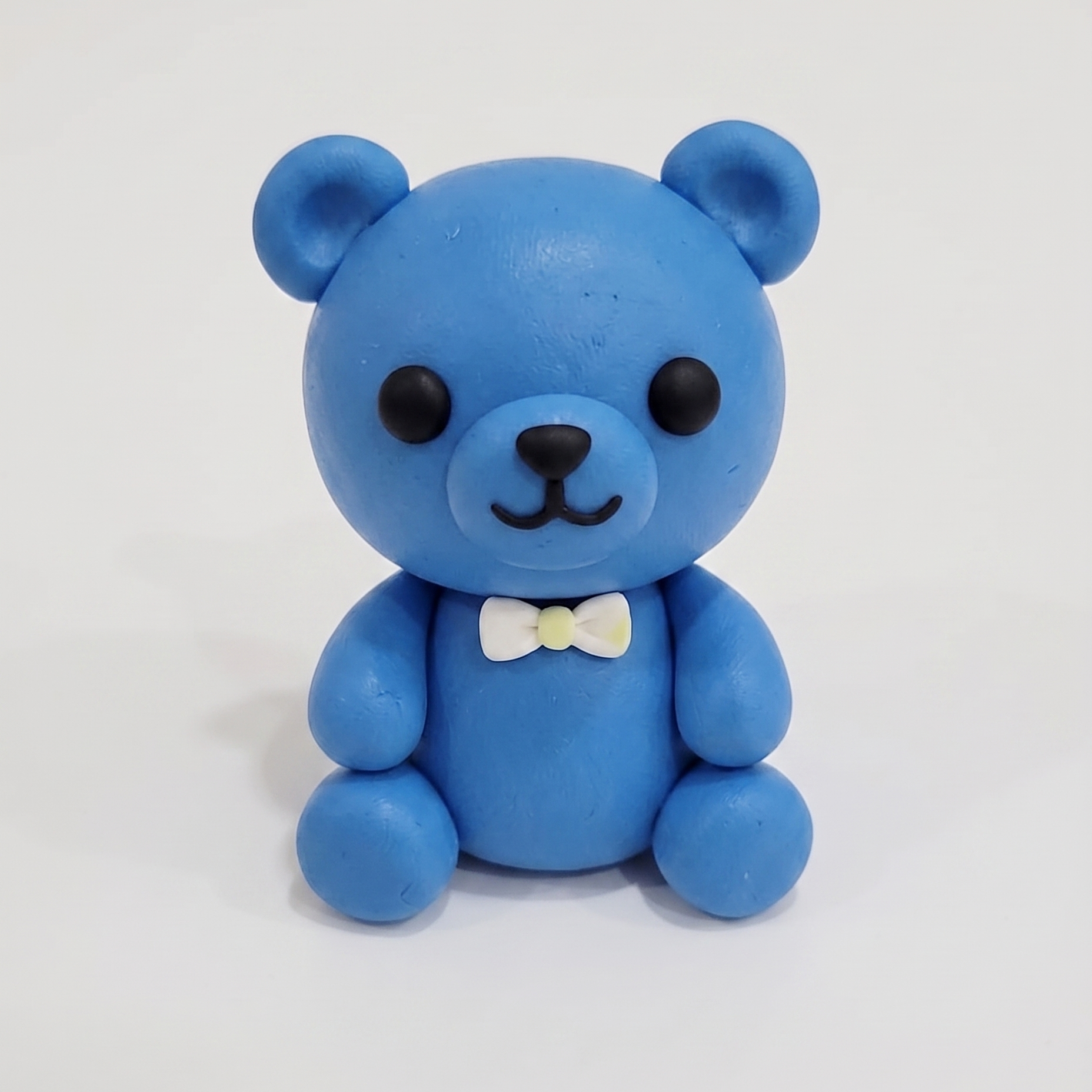 Blue teddy bear figurine with a white bow tie on a white background