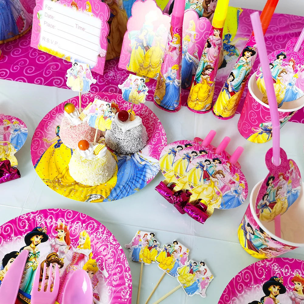 A colorful Disney Princess party table setting with pink plates, cups, straws, napkins, and small cake toppers featuring illustrated princess characters on a white tabletop.